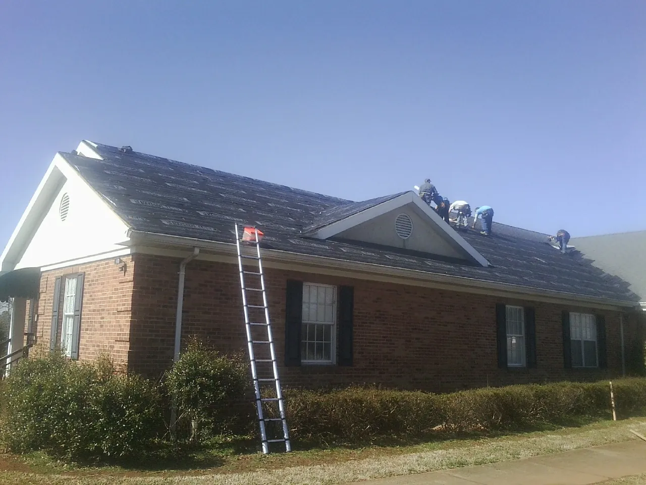 Crew tearing shingles off a brick ranch roof with a ladder set — Metal Roof Repair work by our crew in Mountain Home Afb