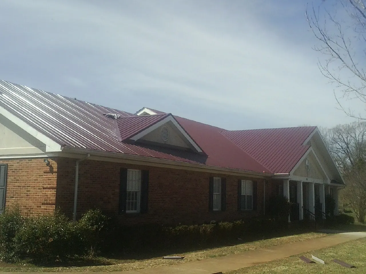Red metal roof with gabled entries on a long brick building, from a Hail Damage Roof Repair job in Mountain Home Afb