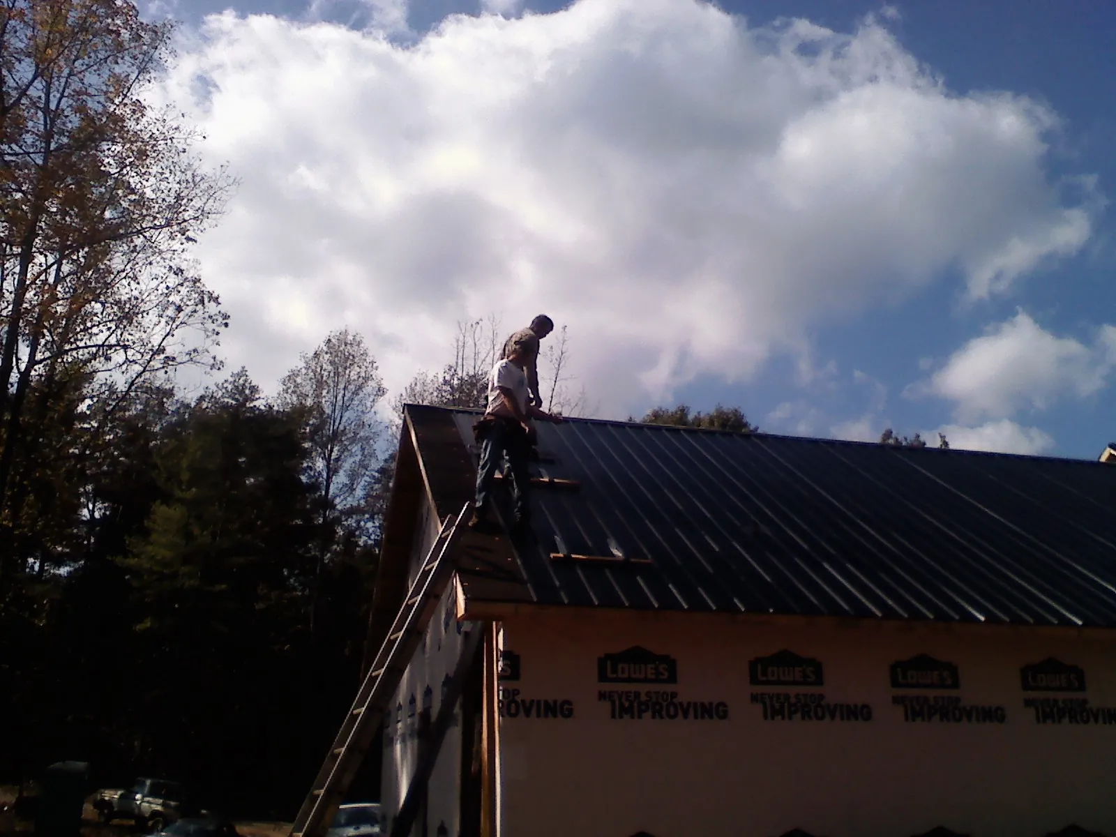 Roofer fastening dark metal panels high against a cloudy sky, from a Roof Inspection job in Mountain Home Afb