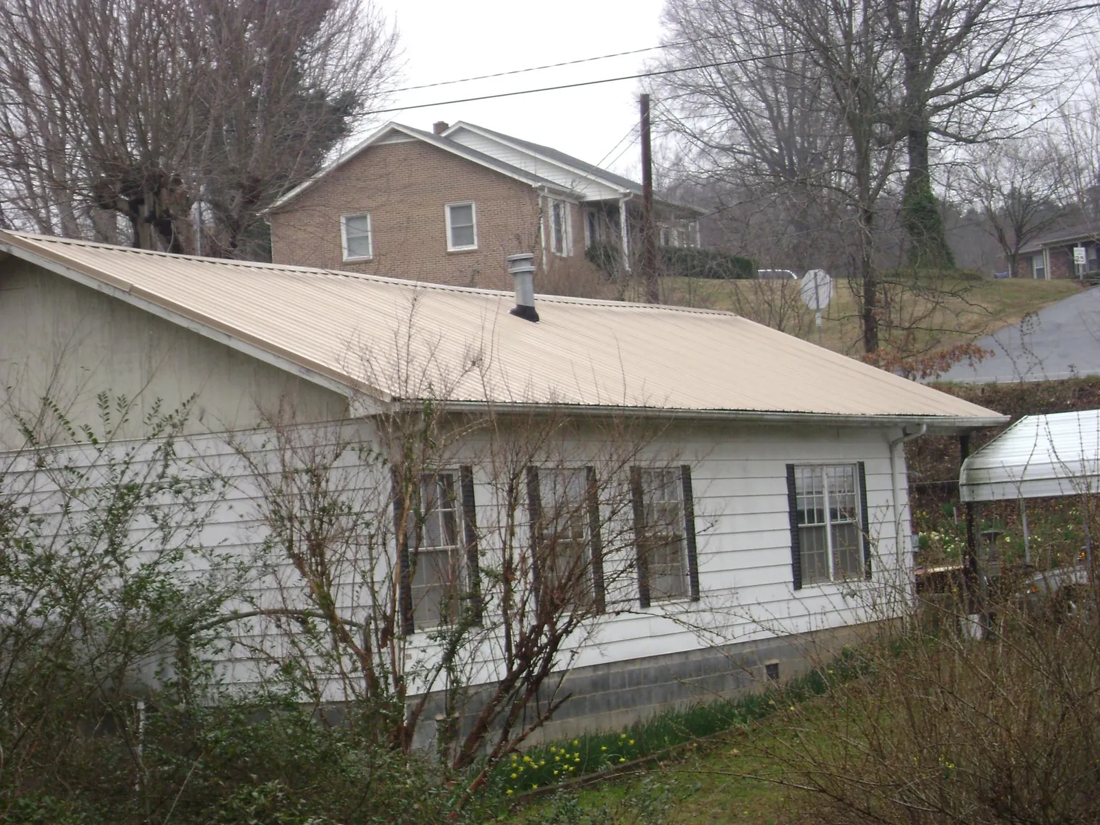 Tan metal roof on a white sided house set into a hillside — Commercial Roofing by Roofing Brothers in Mountain Home Afb